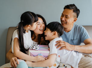 A family unwrapping  a present together on a couch in their home.